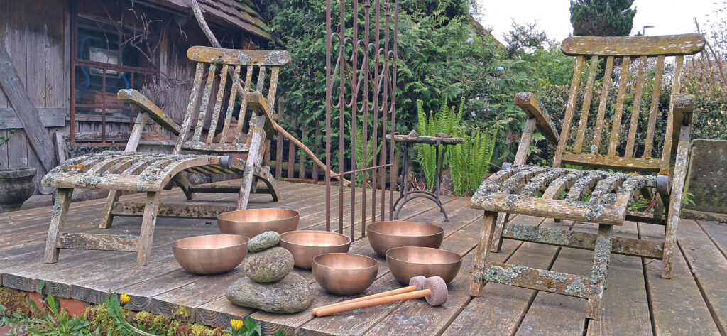 Foto Klangschalen im Garten, daneben zwei Liegen aus Holz