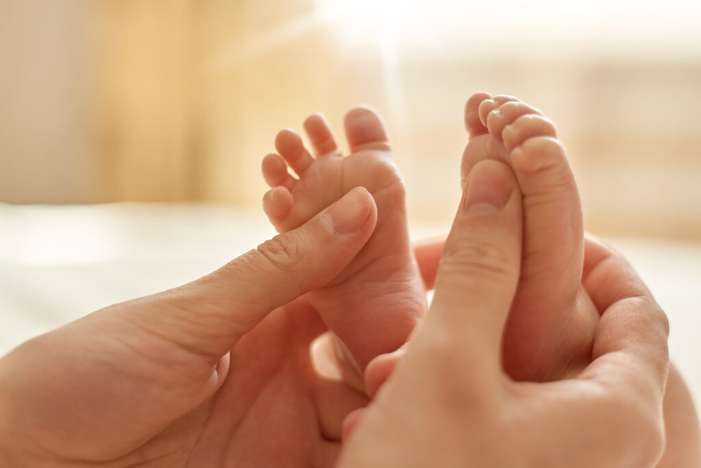 Mutter macht Babymassage bei ihrem Baby und hält die Füßchen in der Hand.